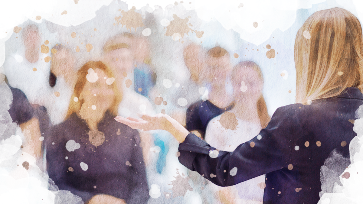 Eine Frau, die etwas vor einem Publikum pr&auml;sentiert und dabei mit einer Hand gestikuliert